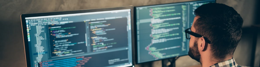 Desenvolvedor trabalhando em código com dois monitores exibindo editor de texto com syntax highlighting