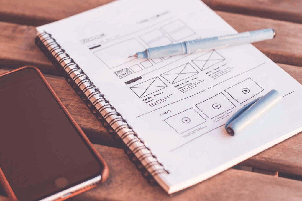 Um caderno com um wireframe de um site desenhado à mão, representando a fase de planejamento que precede o uso de frameworks como o Bootstrap.