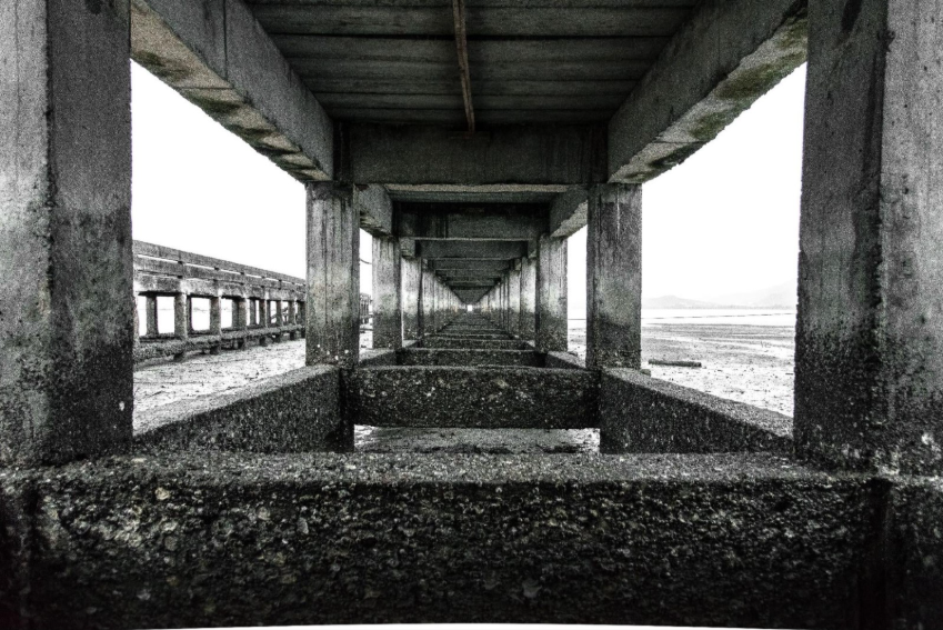 Foto tirada debaixo de um pier de concreto. 