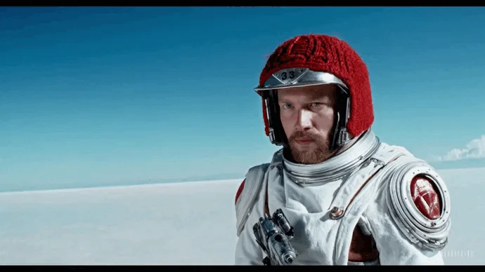o gif representa um astronauta usando um capacete de lã vermelho em um deserto de sal 