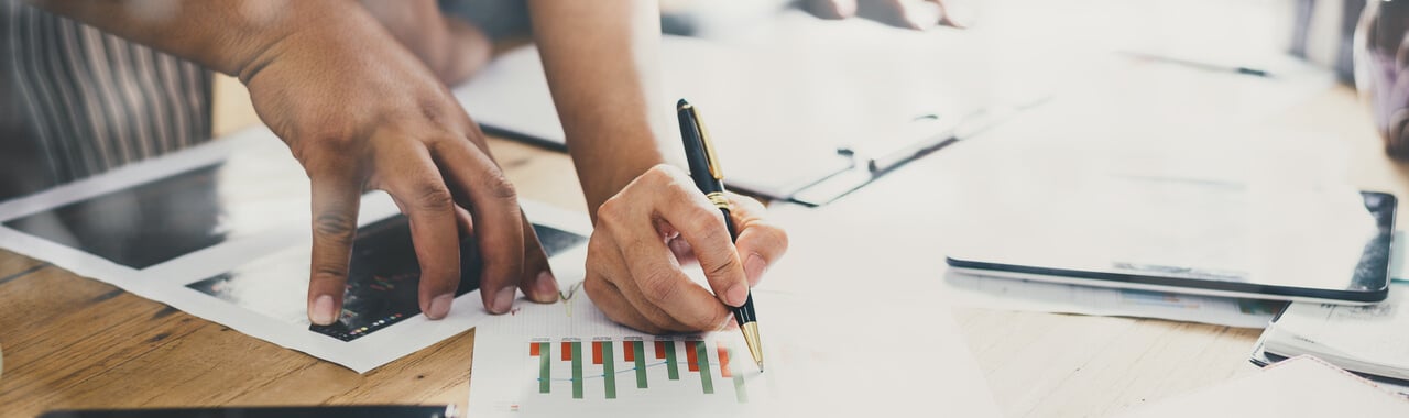 Duas mão sob uma mesa repleta de vários papéis com gráficos espalhados.