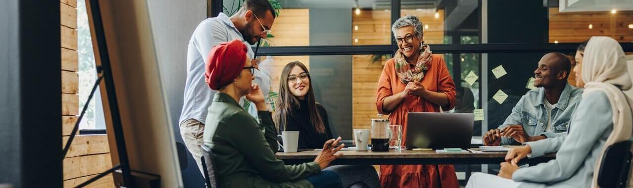 pessoas diversas sentadas em torno de uma mesa com um computador, representando o capital intelectual da empresa
