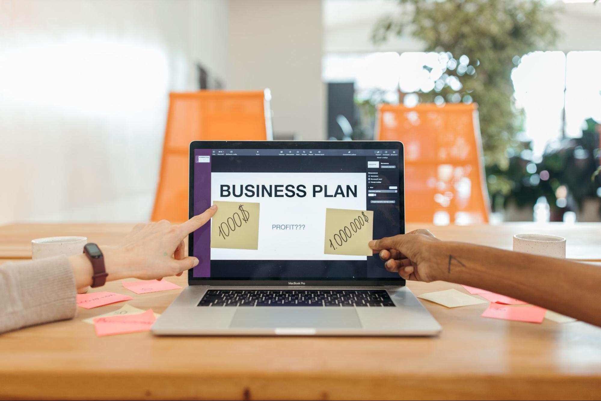 Duas pessoas apontando para a tela do computador, onde está escrito em inglês “Business Plan”.