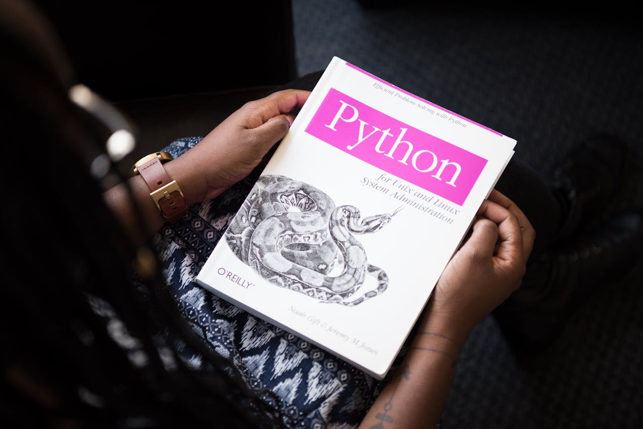 Vista superior de uma pessoa segurando um livro branco e rosa sobre a linguagem de programação Python, com o logo da editora O'Reilly.