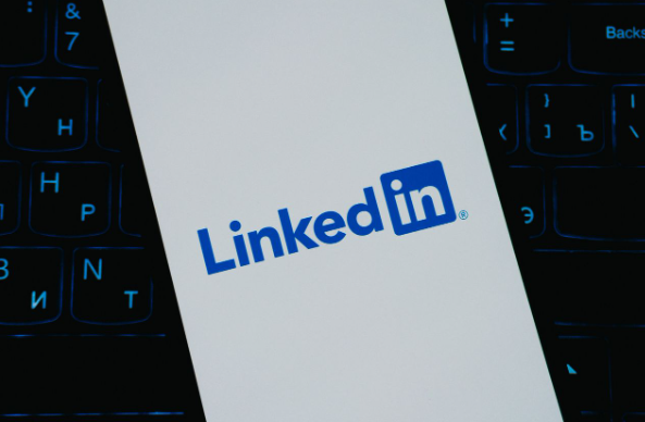 Tela de smartphone com o logo do LinkedIn, apoiada sobre o teclado iluminado de um notebook.