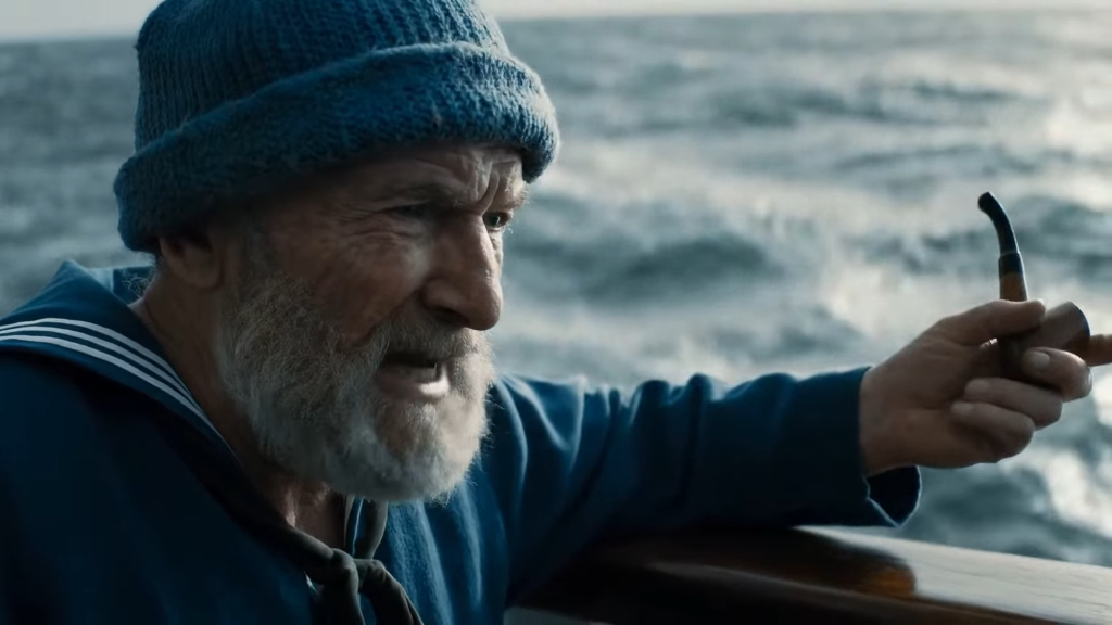 Créditos: Google Veo 3 - Divulgação Oficial | Cena cinematográfica de um marinheiro idoso de gorro azul gesticulando com um cachimbo em um barco, com o mar agitado ao fundo.