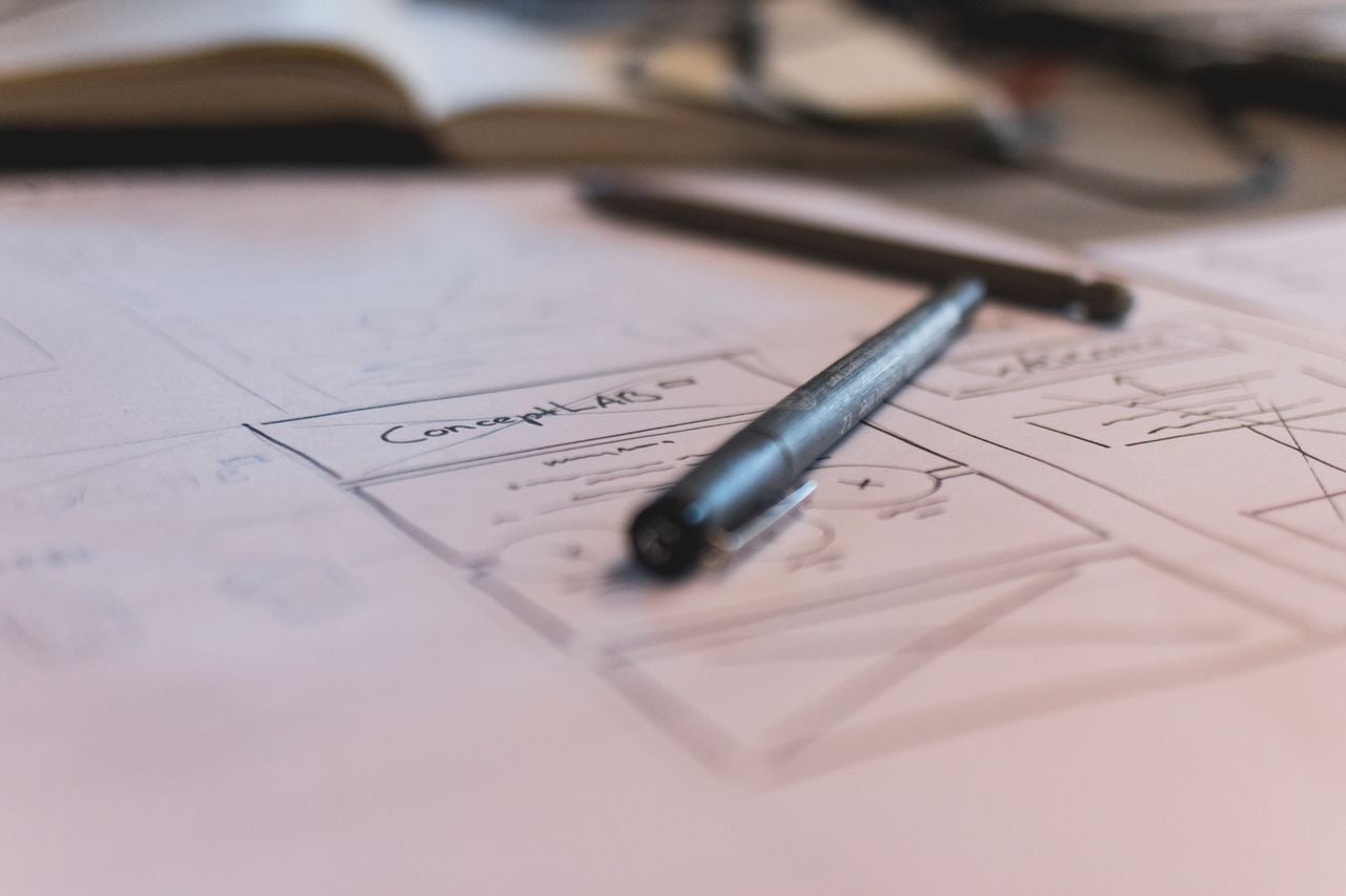 Alt-text: Wireframes de telas desenhados à mão em uma folha de papel, com uma caneta apoiada sobre o rascunho.