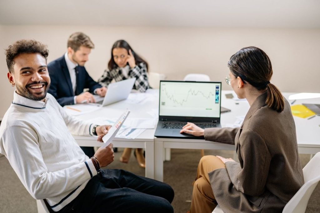 Equipe reunida ao redor de uma mesa com relatórios impressos e um notebook exibindo um gráfico de linha.