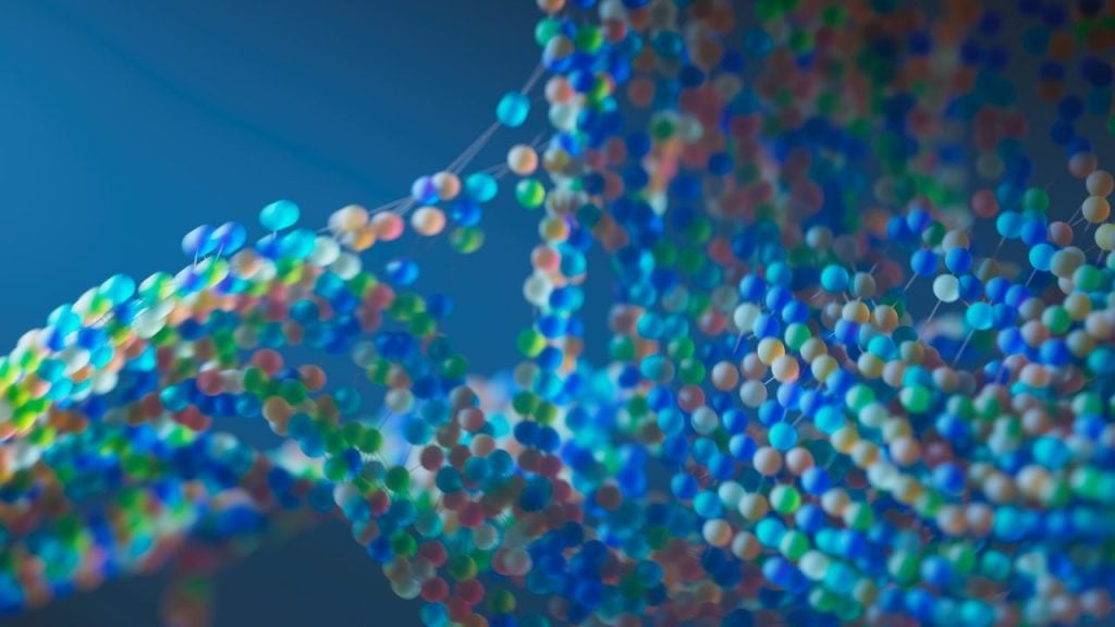 Representação em 3D de uma dupla hélice de DNA formada por milhares de esferas azuis, verdes e alaranjadas em profundidade de campo.